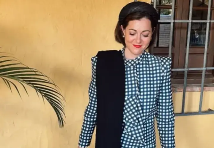 Mujer con traje de cuadros, tocado y bufanda negra. Un ejemplo de dress code elegante para un evento.