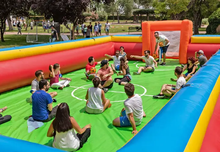 Gente disfrutando de un día familiar en empresas, sentados en un campo de fútbol inflable, riendo y jugando.