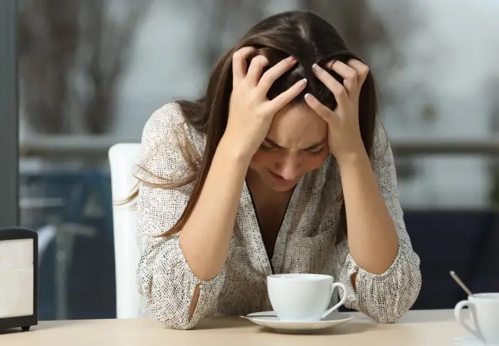Mujer con las manos en la cabeza, mirando su taza de café, quizás porque le doy tantas vueltas a las cosas.
