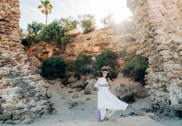 Niña con vestido blanco y corona de flores, posando en unas ruinas, un escenario perfecto para comuniones al aire libre.