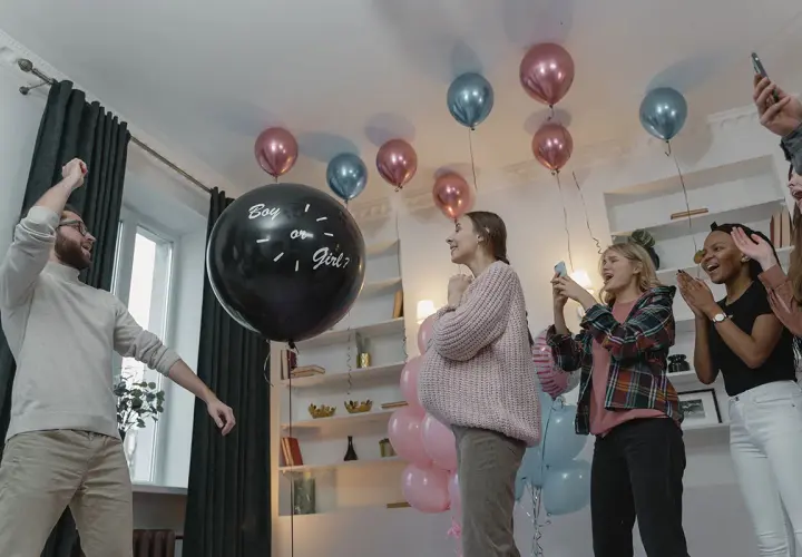 En una fiesta de revelación de género, un hombre levanta el brazo junto a un globo negro que pregunta "Boy or Girl?".