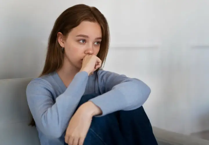 Joven con un bajón emocional, sentada en un sofá, con la mano en la boca y la mirada perdida.