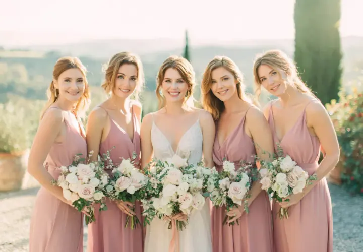 Novia sonriente con su damo de honor, todas con vestidos rosas y ramos de flores.
