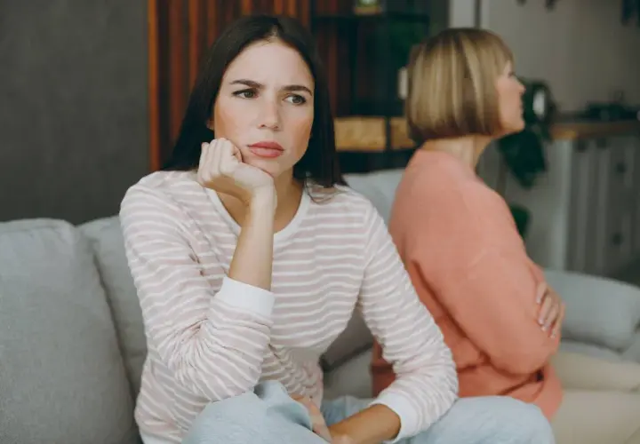 Dos mujeres sentadas en un sofá, una con expresión de aburrimiento, quizás pensando como tratar a una persona que siempre se queja.