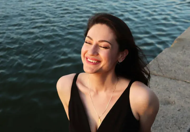 Una mujer sonríe con los ojos cerrados, sintiendo el agradecimiento por un momento de paz junto al agua.