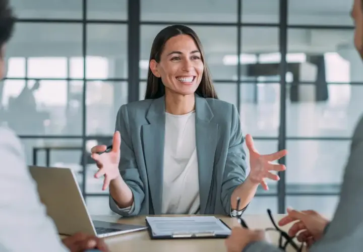 Mujer sonriente explica algo en una reunión. Podría ser un curso de mediación gratis.