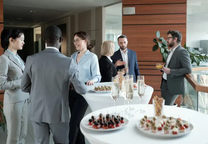 Profesionales conversan y disfrutan de canapés y bebidas en un evento corporativo.