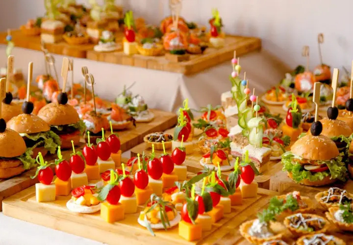 Variedad de aperitivos para bodas: mini hamburguesas, canapés de salmón, brochetas de tomate y queso, y tartas saladas. ¡Un festín visual!