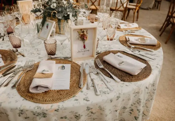 Mesa de boda con manteles florales, vajilla y centros de mesa rústicos.