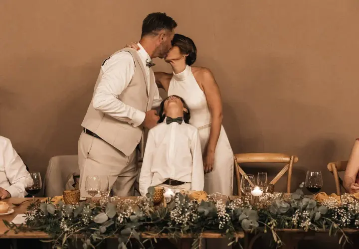 Una pareja se besa tiernamente mientras su hijo mira al cielo, celebrando bodas de plata, oro y platino.