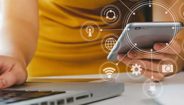 Persona usando un móvil y portátil con iconos de analítica digital superpuestos.