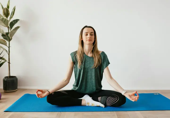 Mujer meditando en postura de loto sobre una esterilla azul. Practica 8 ejercicios de respiración para relajarse.