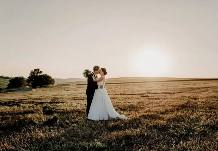 Novios besándose en un campo dorado al atardecer, un hermoso escenario para bodas en mayo.