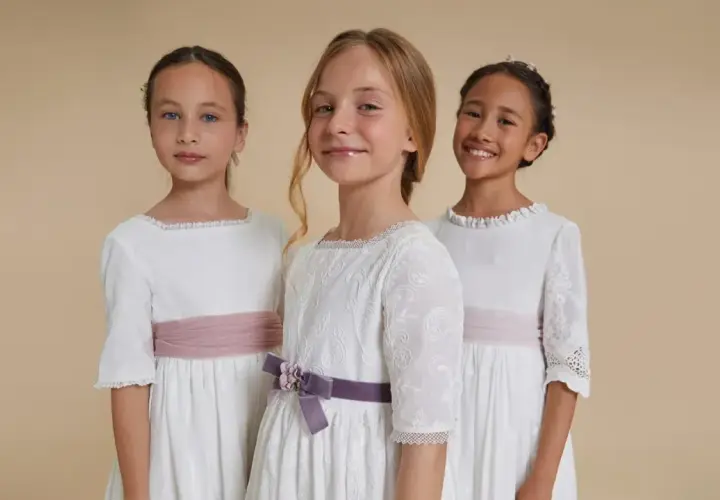 Tres niñas con vestidos blancos de comunión, cinturones rosas y morados. Ideas para sorprender a una niña en su comunión.