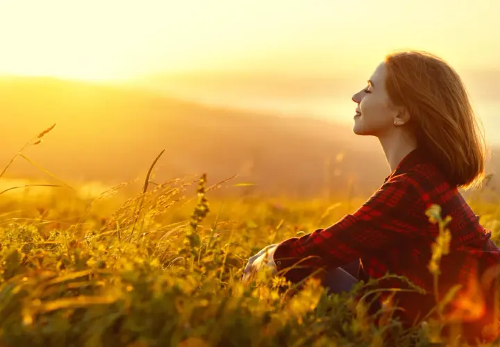 Mujer sonríe en un campo al atardecer, disfrutando de la paz y fortaleciendo su autoestima personal.