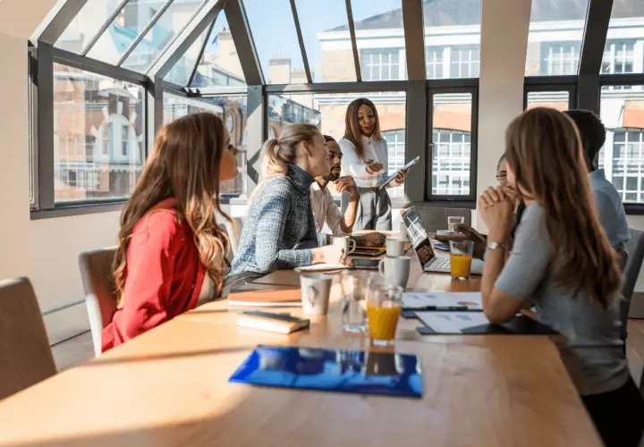 Un grupo diverso de profesionales participa en un workshop, discutiendo ideas alrededor de una mesa con laptops y bebidas.