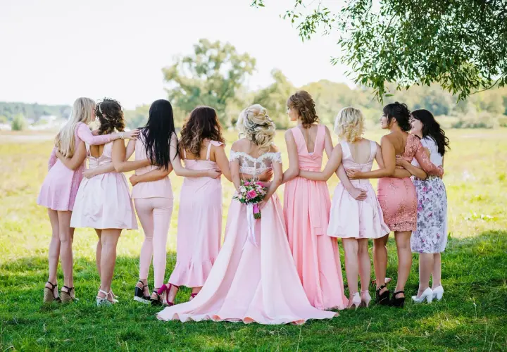 Novia rodeada por sus damas de honor, todas vestidas de rosa, en un campo verde.