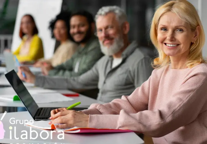Mujeres y hombres participan en un curso formador de formadores online. Sonríen mientras aprenden en un aula moderna.