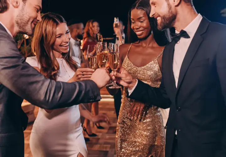 Pareja brinda con champán en una fiesta elegante. Ella luce un vestido dorado brillante, un look perfecto para una **black tie mujer**.