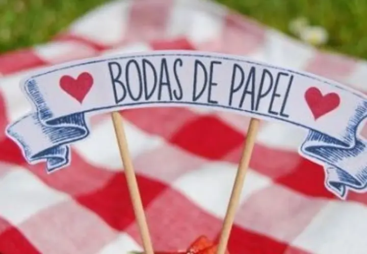 Un letrero de "Bodas de Papel" con corazones rojos, sobre un mantel de cuadros rojos y blancos.