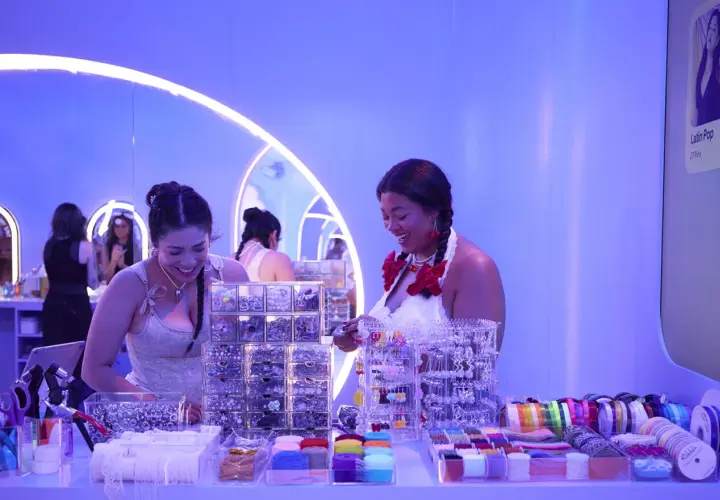 Dos mujeres sonríen en un puesto de accesorios para el cabello y cintas, parte de eventos de marca.