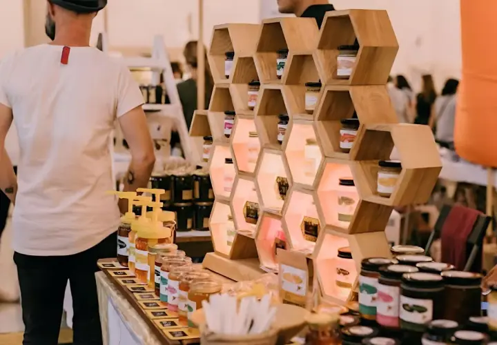 Exhibición de mieles artesanales en ferias empresariales. Tarros de miel en estanterías de madera con forma de panal, iluminados.