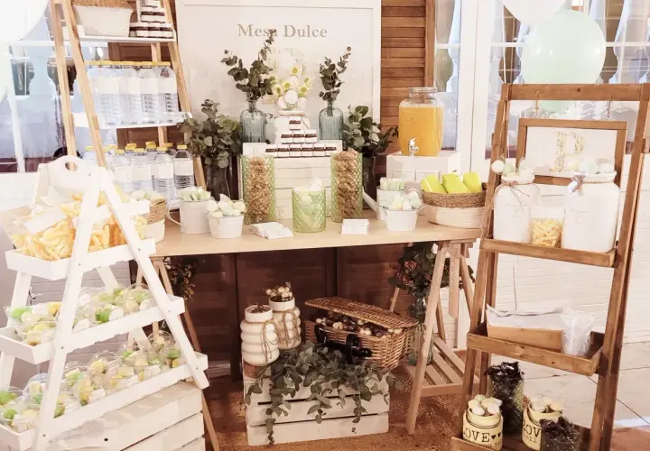 Un candy bar rústico con dulces, botellas de agua y un cartel "Mesa Dulce".