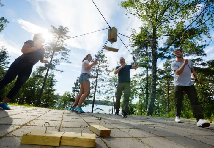 Un grupo participa en un juego de team building outdoor, tirando de cuerdas para mover un objeto de madera.