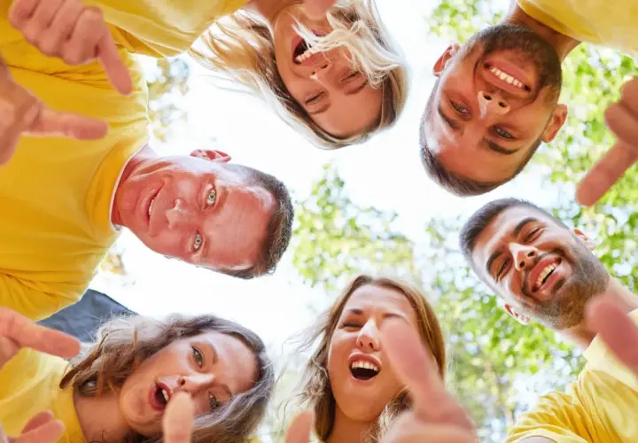 Un grupo de personas sonríe y señala hacia abajo, fomentando el espíritu de equipo. ¡Perfecto para dinamicas de grupo para empresas!