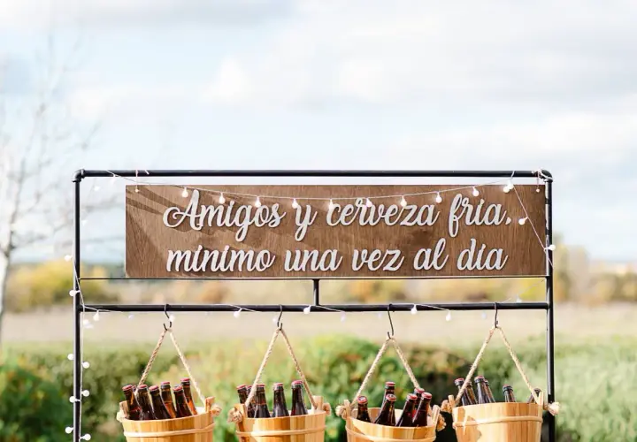 Decoración barra libre boda: letrero "Amigos y cerveza fría, mínimo una vez al día" sobre cubos de cerveza.