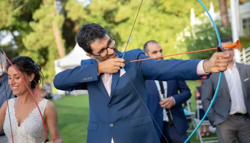 Novio con arco y flecha, parte de los juegos de bodas. La novia sonríe a su lado.