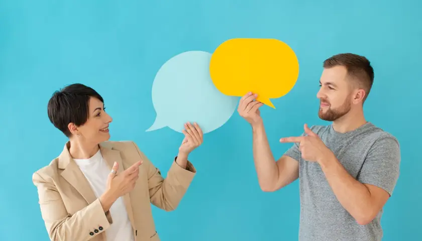 Hombre y mujer con bocadillos de diálogo, discutiendo ideas. Sonrisas y gestos sugieren técnicas para no entrar al trapo en una conversación.