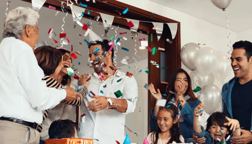 Familia celebrando fiestas sorpresa con confeti y globos. Todos ríen y se abrazan, creando un ambiente de alegría.