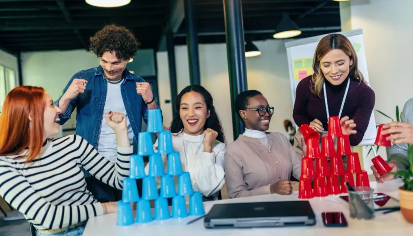 Equipo celebrando en juegos de empresa, apilando vasos de colores.