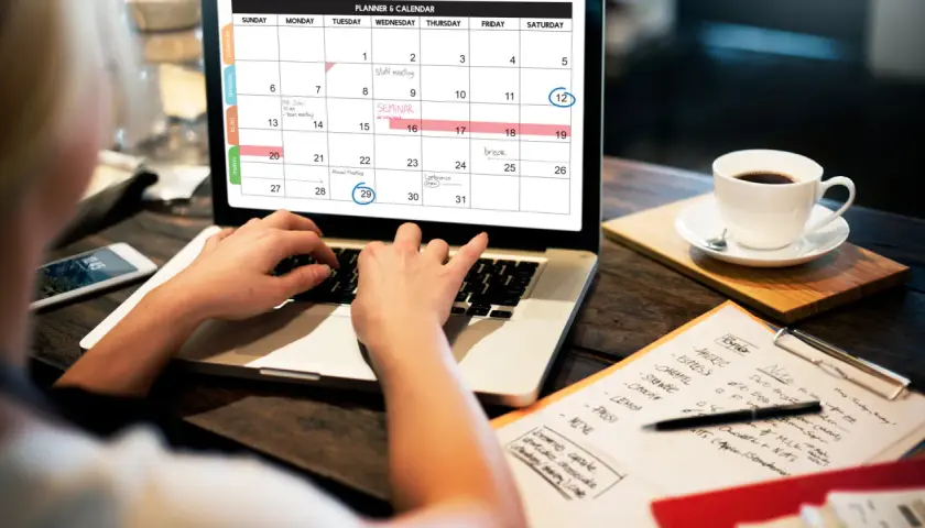 Persona organiza su **curso gestión administrativa** en un calendario digital, con una taza de café al lado.