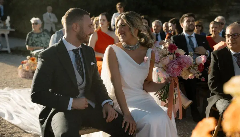 Novios sonrientes en su **matrimonio express**. Ella, radiante con vestido blanco y ramo de flores. Él, elegante de traje oscuro.