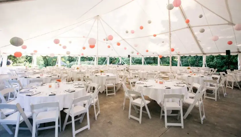 Carpa blanca con mesas redondas y sillas blancas, decorada con farolillos de colores. Un espacio ideal para **sitios de eventos**.