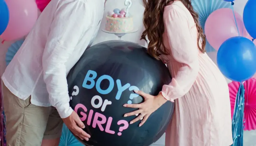 Pareja celebra un gender reveal, con un globo negro que pregunta "BOY or GIRL?".