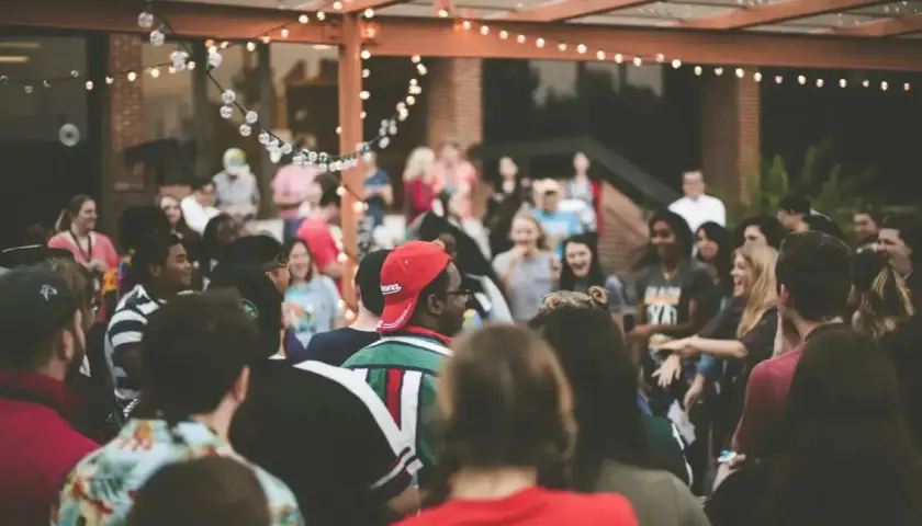 Grupo de personas disfrutando en una fiesta al aire libre, con luces decorativas. ¡Excelentes ideas para cenas de empresa!