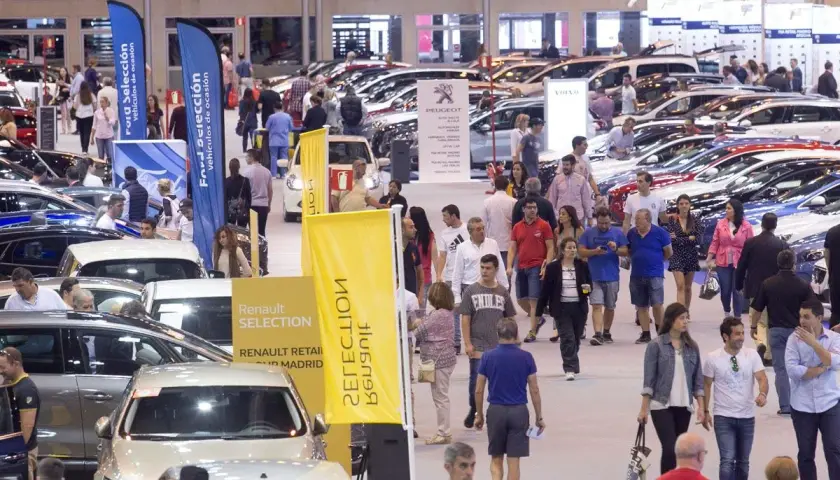 Gente paseando entre coches en una feria comercial. Banderolas de Ford y Renault anuncian vehículos de ocasión.