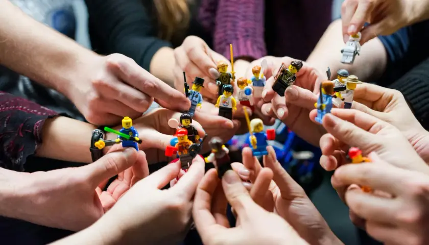 Manos sostienen figuras de Lego, creando un ambiente de **actividades team building originales** y divertidas.