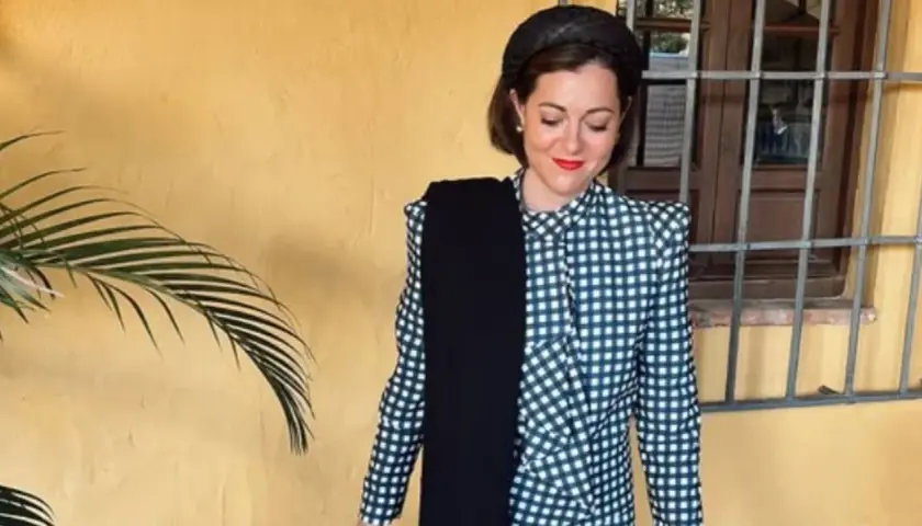 Mujer con traje de cuadros, tocado y bufanda negra. Un ejemplo de dress code elegante para un evento.