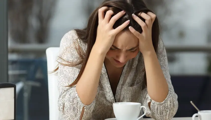 Mujer con las manos en la cabeza, mirando su taza de café, quizás porque le doy tantas vueltas a las cosas.