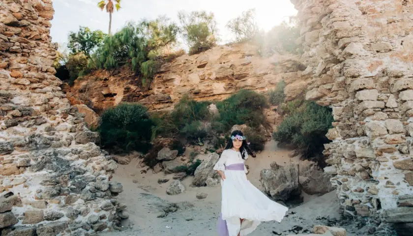 Niña con vestido blanco y corona de flores, posando en unas ruinas, un escenario perfecto para comuniones al aire libre.