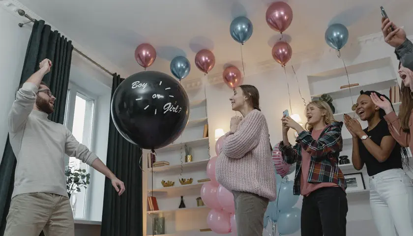 En una fiesta de revelación de género, un hombre levanta el brazo junto a un globo negro que pregunta "Boy or Girl?".