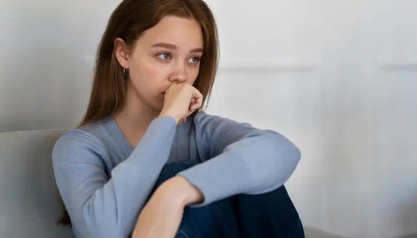 Joven con un bajón emocional, sentada en un sofá, con la mano en la boca y la mirada perdida.