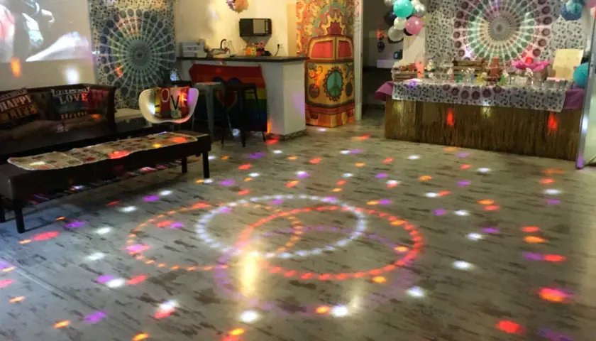 Un salón decorado con estilo hippie para unas **fiestas de cumpleaños de adultos divertidas**. Luces de discoteca proyectan círculos de colores sobre el suelo.