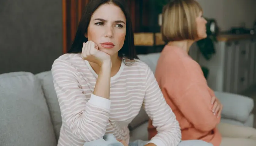 Dos mujeres sentadas en un sofá, una con expresión de aburrimiento, quizás pensando como tratar a una persona que siempre se queja.