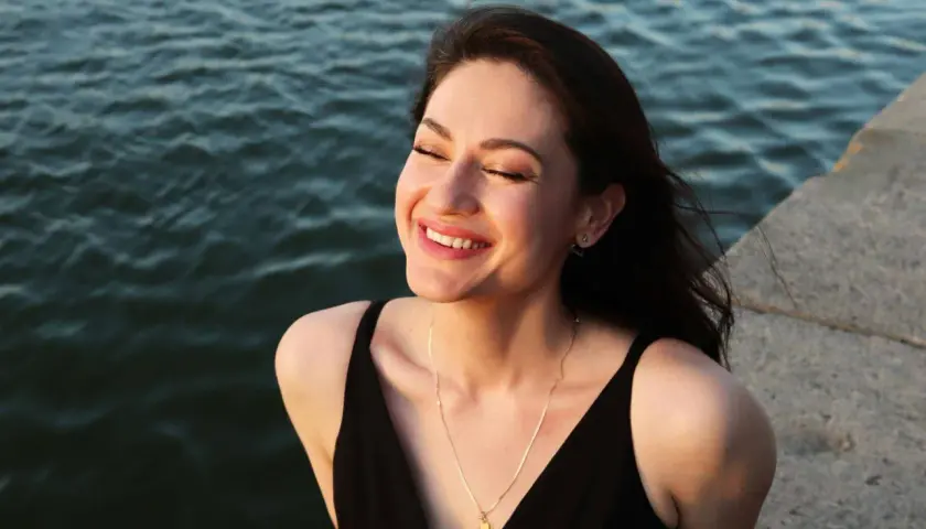 Una mujer sonríe con los ojos cerrados, sintiendo el agradecimiento por un momento de paz junto al agua.