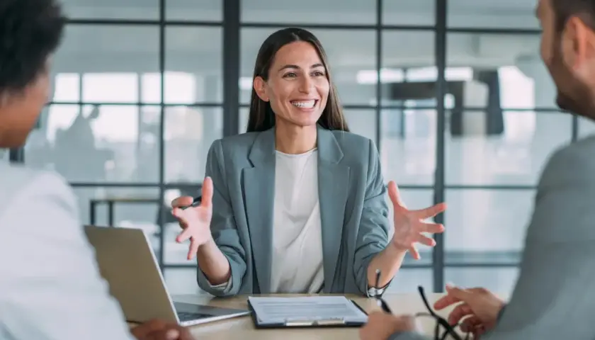 Mujer sonriente explica algo en una reunión. Podría ser un curso de mediación gratis.